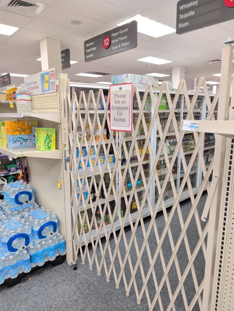 An aisle of a convience store entirely blocked off by a white gate. Behind the gate, some cans and bottles of alcohol can be seen.