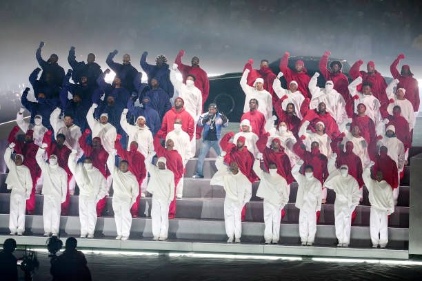kendrick lamar and dancers at his half time show. their clothing and arrangement makes it look like an american flag and the dancers are holding a fist in the air while kendrick is singing in the middle