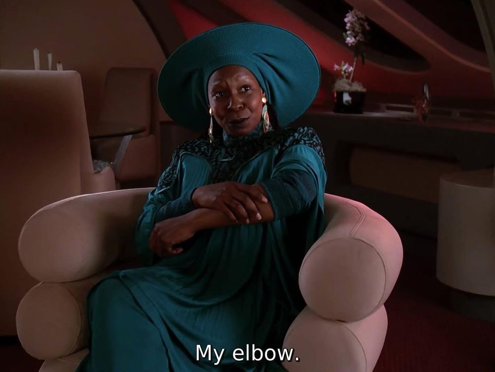 TNG; "Suspicions"; Guinan sitting in Bev's quarters, clutching her arm, with caption: My elbow.