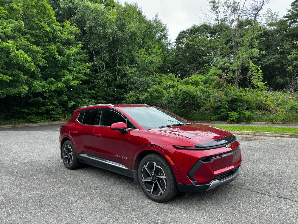 2024 Chevrolet Equinox 2LT EV in Radiant Red Tintcoat with a forest behind her