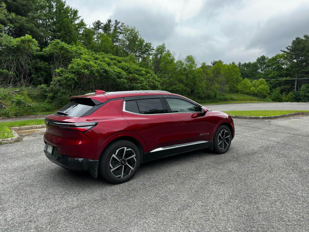 2024 Chevrolet Equinox 2LT EV in Radiant Red Tintcoat with a forest behind her