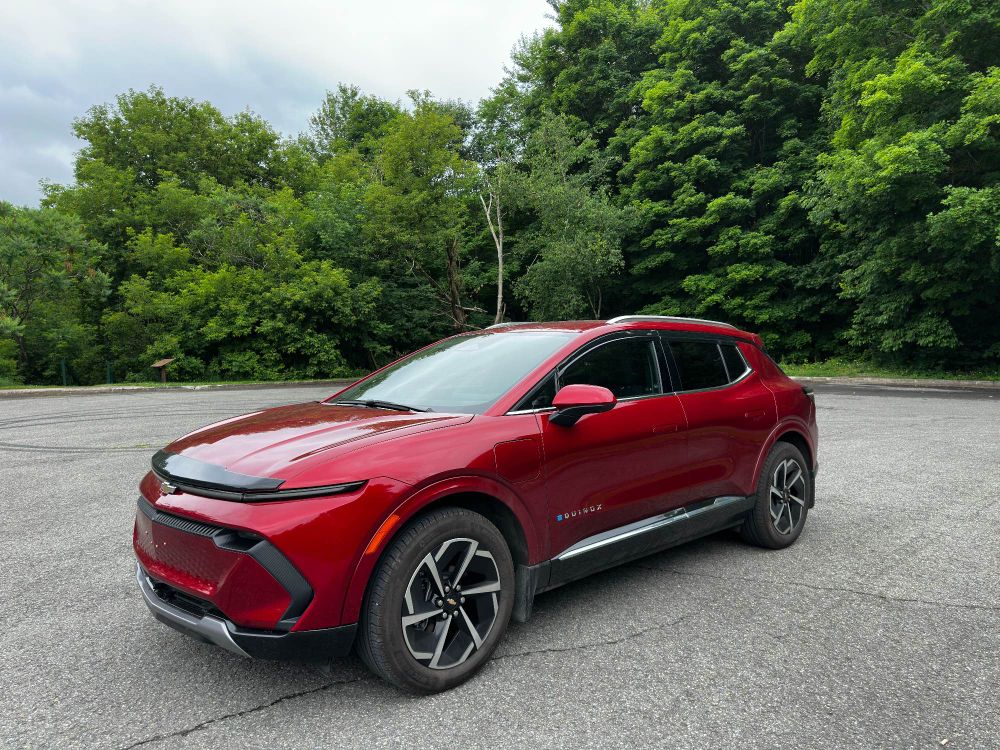 2024 Chevrolet Equinox 2LT EV in Radiant Red Tintcoat with a forest behind her