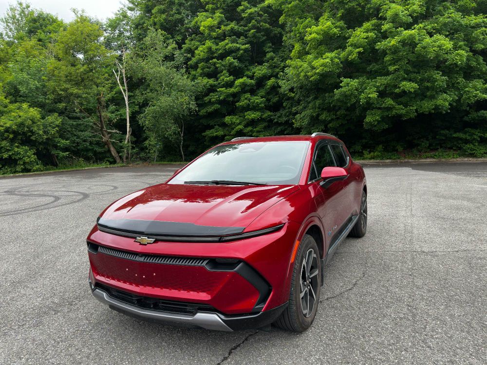 2024 Chevrolet Equinox 2LT EV in Radiant Red Tintcoat with a forest behind her