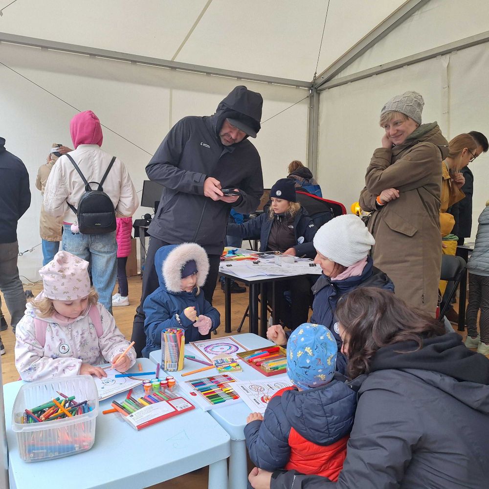Inside the science-fair tent, bundled-up children colour astronomy worksheets at low tables while parents and other visitors observe the activities.