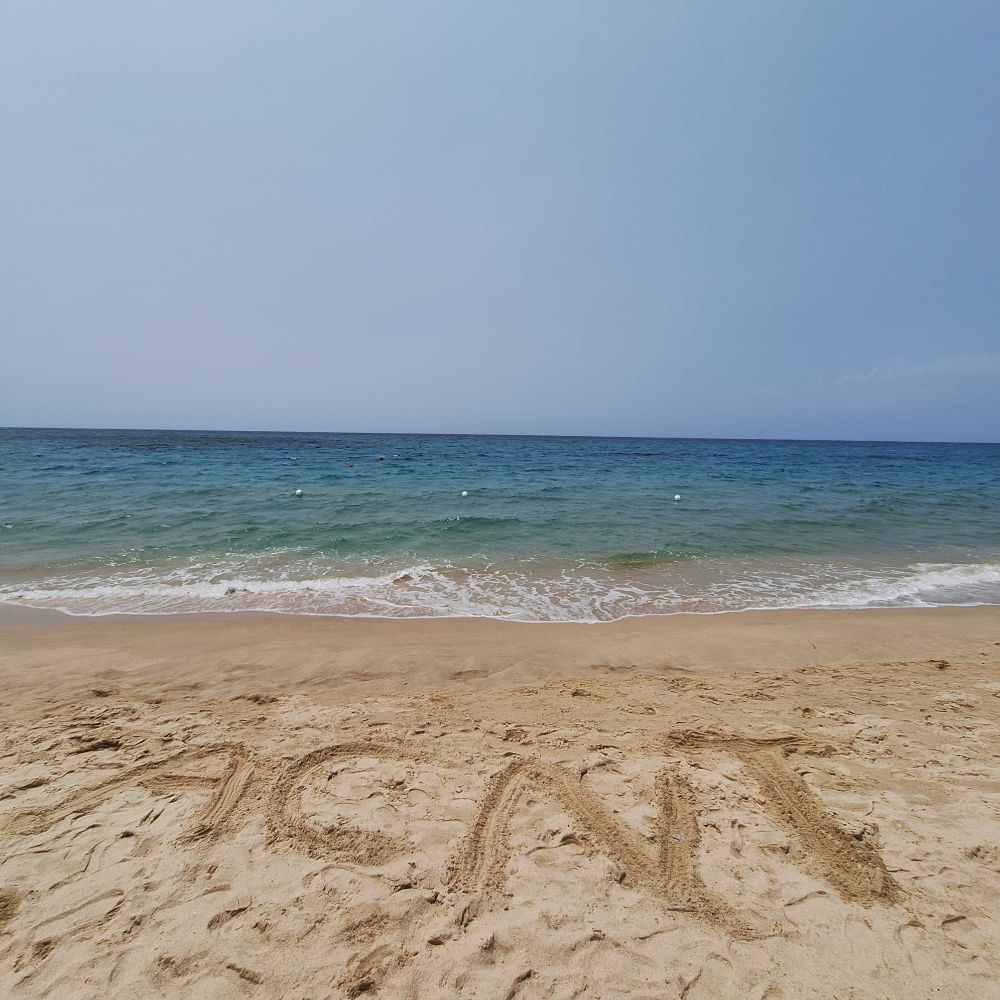 A calm seashore in Sardinia with ‘ACNT’ written in the sand.