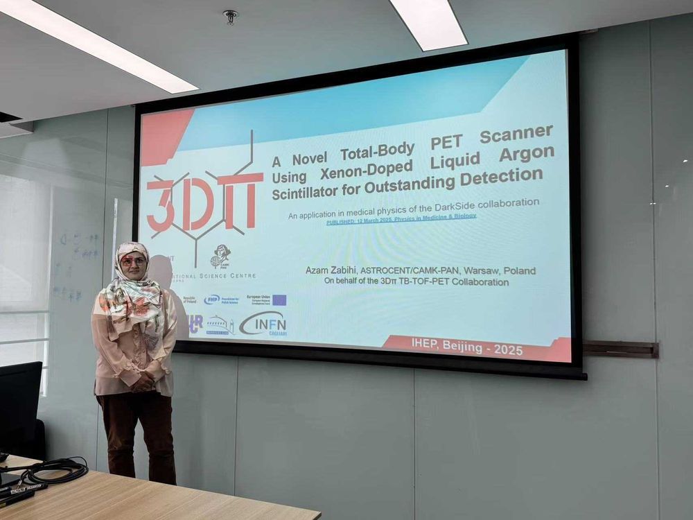 A researcher in a patterned headscarf stands next to a large presentation screen showing the title: ‘A Novel Total-Body PET Scanner Using Xenon-Doped Liquid Argon Scintillator for Outstanding Detection.’ Logos of collaborating institutions and projects are visible at the bottom.