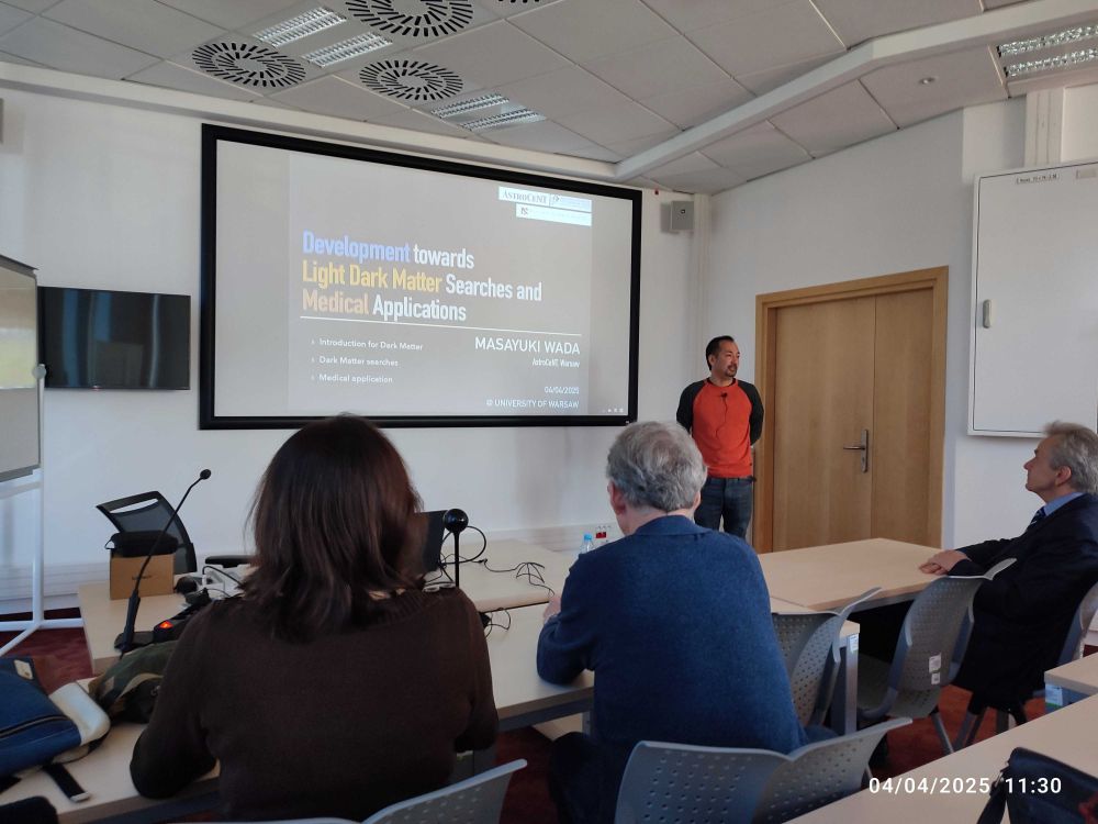  A speaker stands at the front of a lecture room presenting a talk titled "Development towards Light Dark Matter Searches and Medical Applications." The slide is projected on a large screen, and several attendees are seated and listening attentively. The event takes place at the University of Warsaw on April 4, 2025.