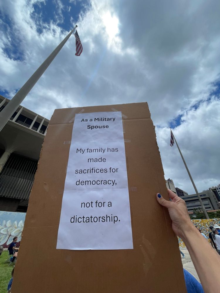 Sign says: 
As a military spouse, my family has made sacrifices for democracy, not dictatorship.