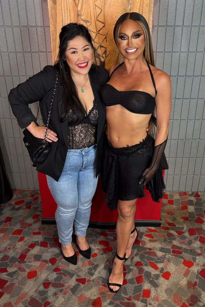 Photo of two stunning women wearing black but let’s acknowledge the sickening season 15 winner of RuPaul’s Drag Race and forever mother, Sasha Colby and y’all better not come for my muffin top because I enjoyed my banh mi earlier and have no regrets lol