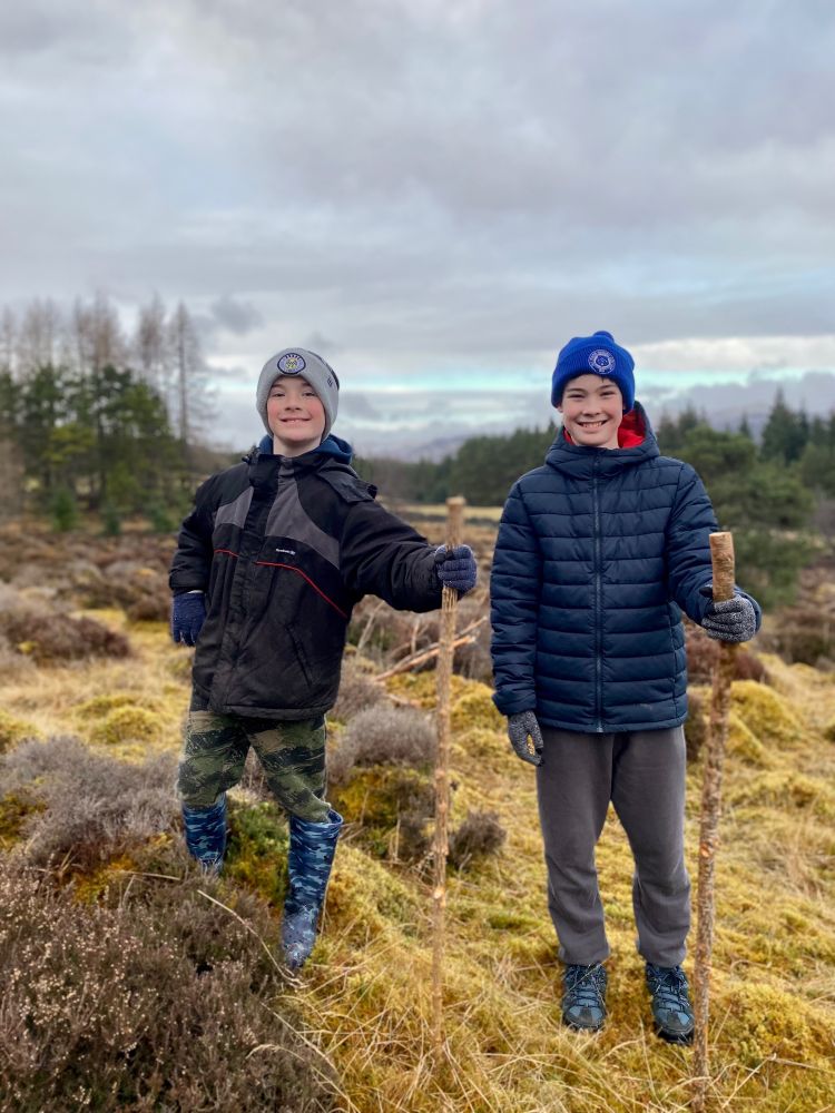 Two boys smiling in the moorland holding walking sticks 