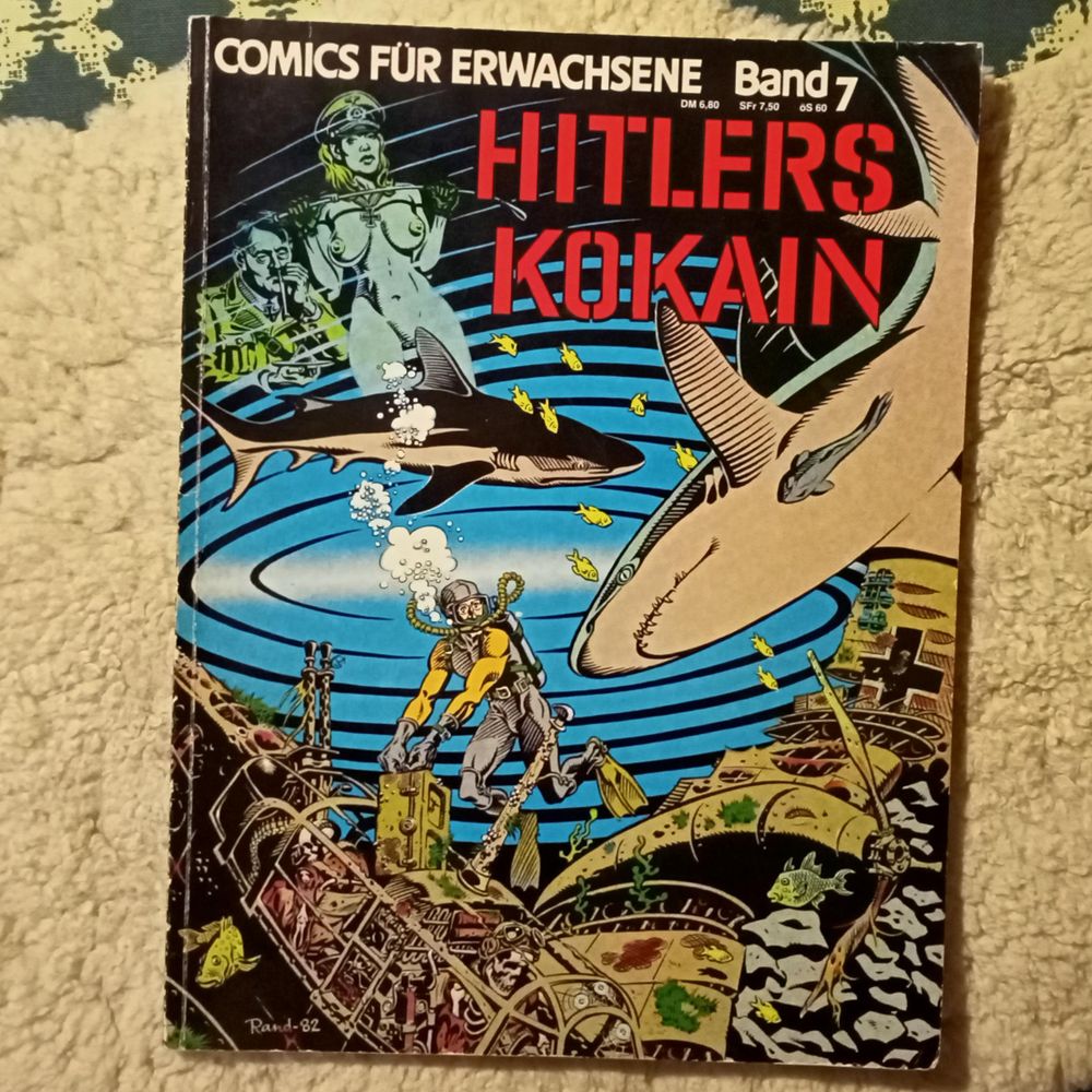 Ein Comicalbum. Wir sehen einen Taucher, der gerade aus einem abgestürzten Flugzeug am Meeresboden, in dessen Cockpit Skelette zu sehen sind, eine Metallkiste birgt und dabei bemerkt, dass ihn zwei Haie umkreisen. Im Bildhintergrund ist Adolf Hitler zu sehen, der gerade eine Line Koks zieht, und vor ihm eine nackte Frau. Sie blickt uns abschätzig an und lässt eine Reitgerte zwischen den behandschuhten Händen federn. Sie hat eine Schirmmütze der Luftwaffe auf und ein eisernes Kreuz um den Hals. Titelei: "Comics für Erwachsene / Band 7 / Hitlers Kokain".