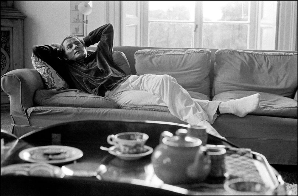 Shaw lies back on the couch in his living room. In the foreground, an out-of-focus tray with a pot of tea & teacup.