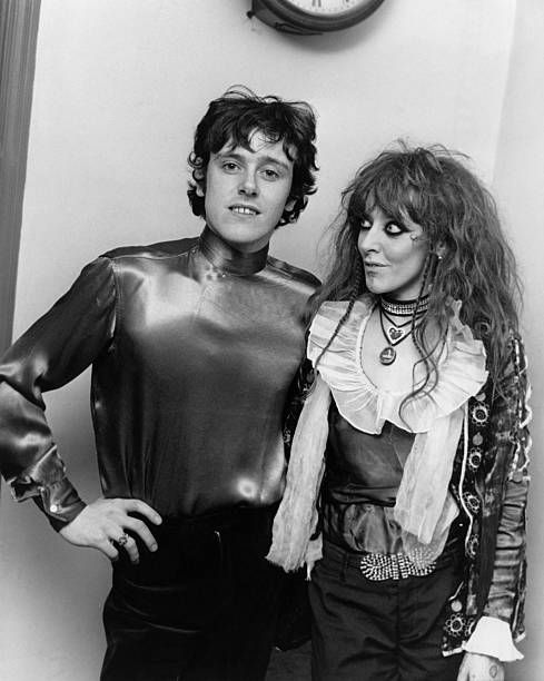 The two stand together, wearing the latest Swinging London outfits.