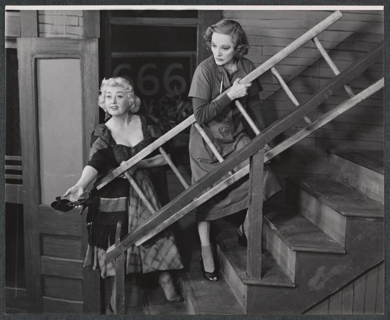 The two try to one-up each other as they, for some reason, carry a ladder up a flight of stairs.