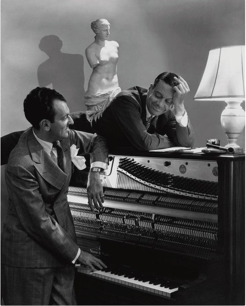 Hart at the piano keybord, with Porter leans against the back of the instrument. Behind them, an armless Greek statue.