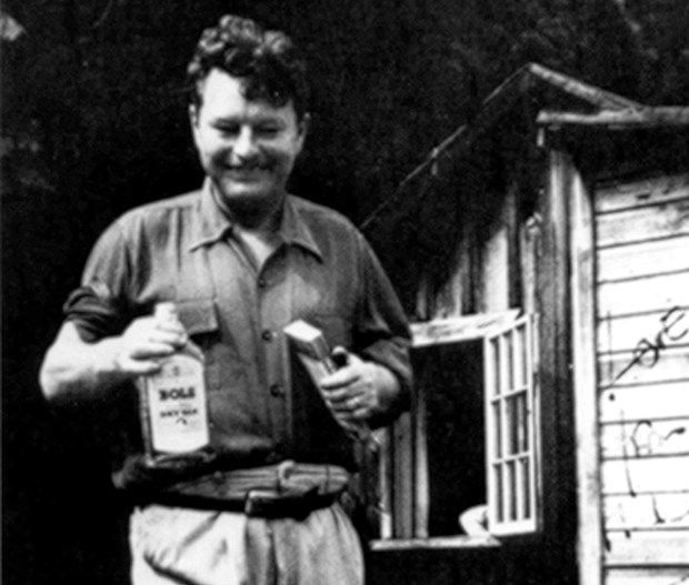 Lowry with a book and a bottle of Bols gin, in front of his beach cabin.
