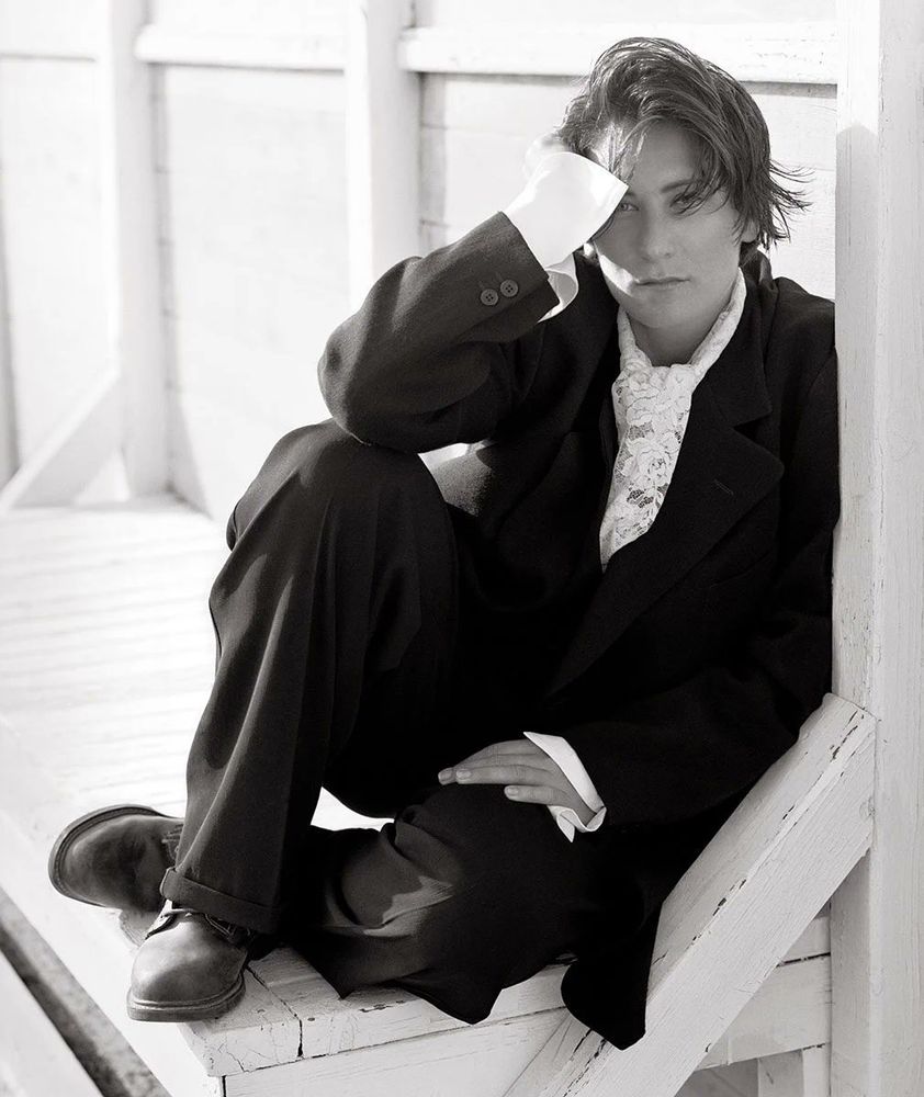 lang in a black suit, with a frilly white shirt