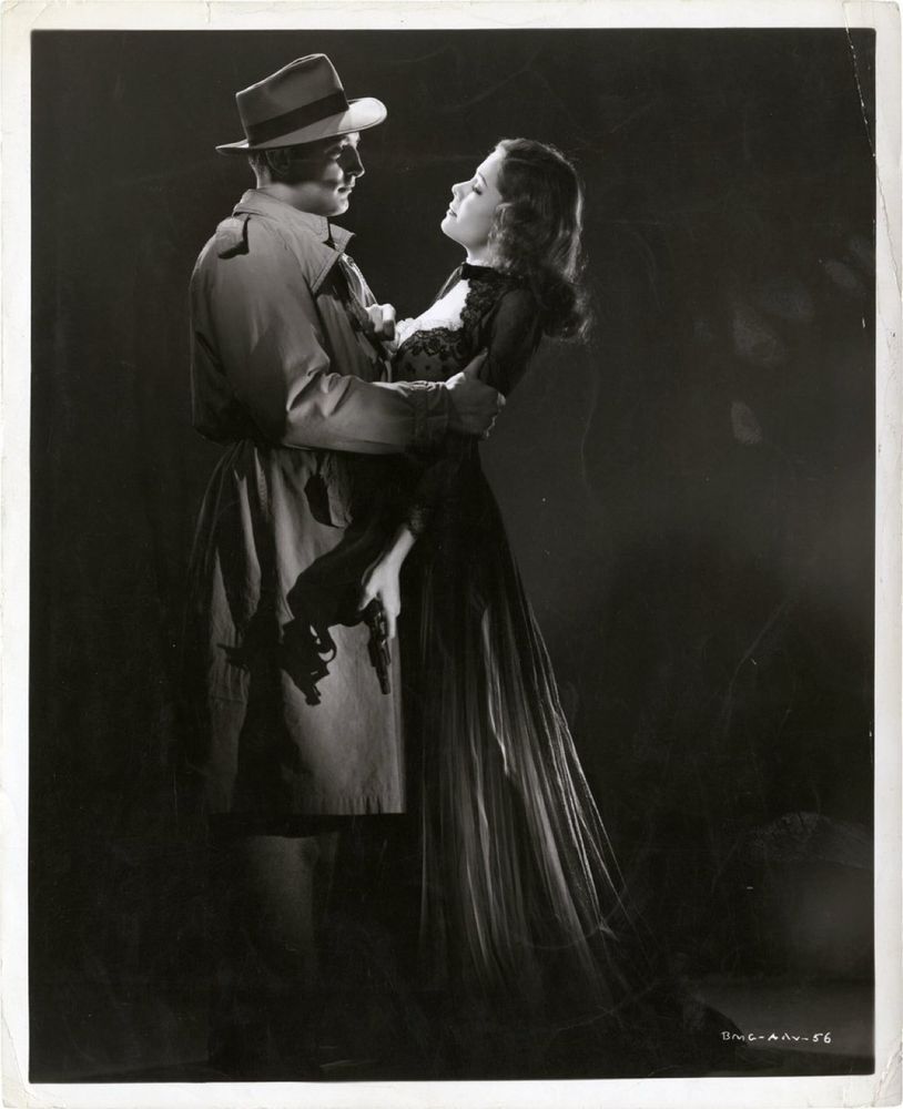 Mitchum & Greer in a clinch, perfectly lit. She’s wearing a long black dress & has a gun in her hand. He’s in a trench coat & hat and knows he doesn’t need to worry about the gun. 