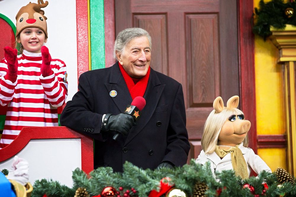 A smiling Bennett in an overcoat & red scarf, proudly standing next to Miss Piggy at the parade