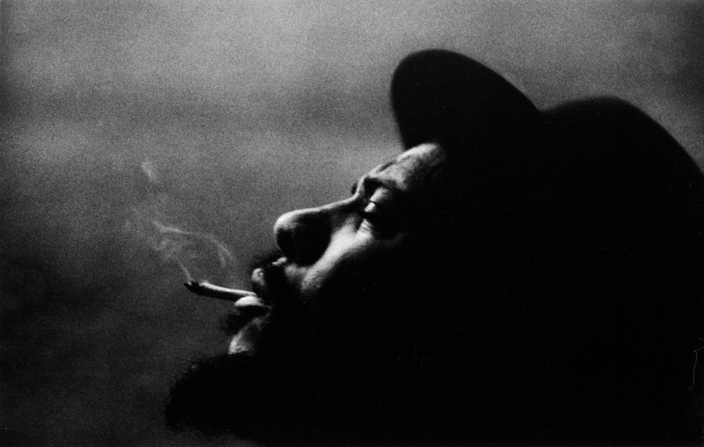 Closeup of Monk in profile. His head is back & he's smoking a cigarette.