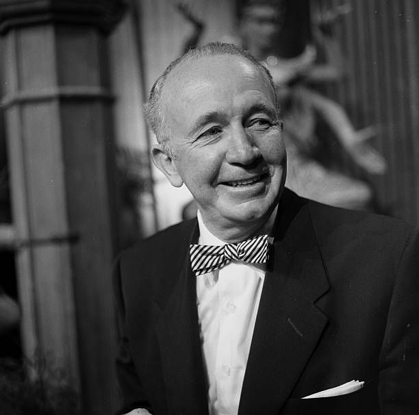 Brennan smiles at a party, wearing a suit & striped bowtie.