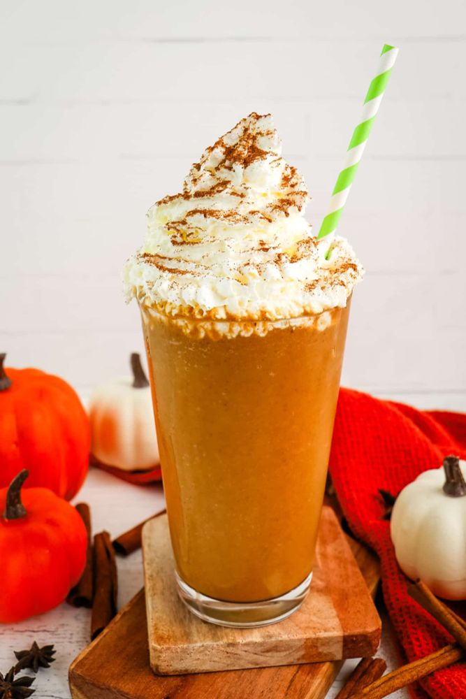 A homemade pumpkin spice frappechino with a green and white straw. Bg has orange and white pumpkins, cinnamon and those star spices I don't know the name of. There's also a red blanket