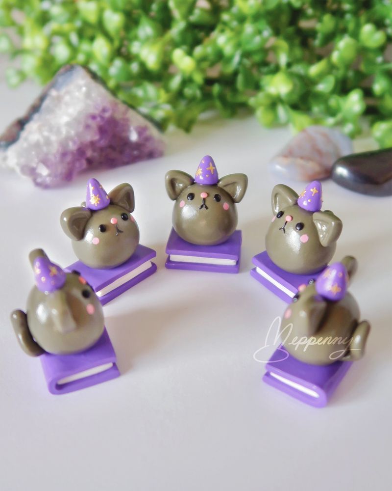 Handmade miniature clay cats wearing tiny wizard hats and sitting on books, arranged in a circle facing each other