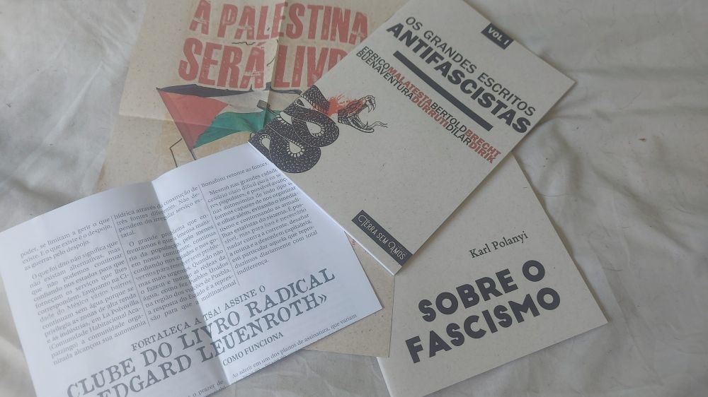 Um "spread" contendo os livros "Sobre o Fascismo", de Karl Polanyi e "Os Grandes Escritos Antifascistas" de vários autores; um pôster "A Palestina Será Livre" e um panfleto do Clube do Livro Radical "Edgar Leuenroth".