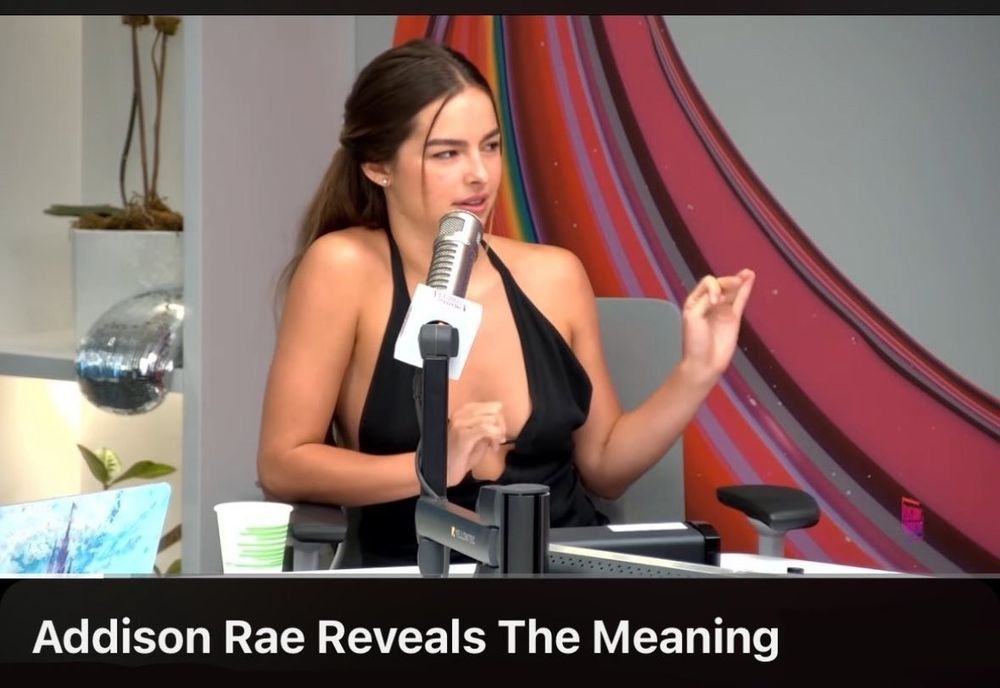 Addisson Rae reveals the meaning, é a imagem de uma mulher branca com uma brusa preta e um decote profundo gesticulando como quem está literalmente explicando algo 