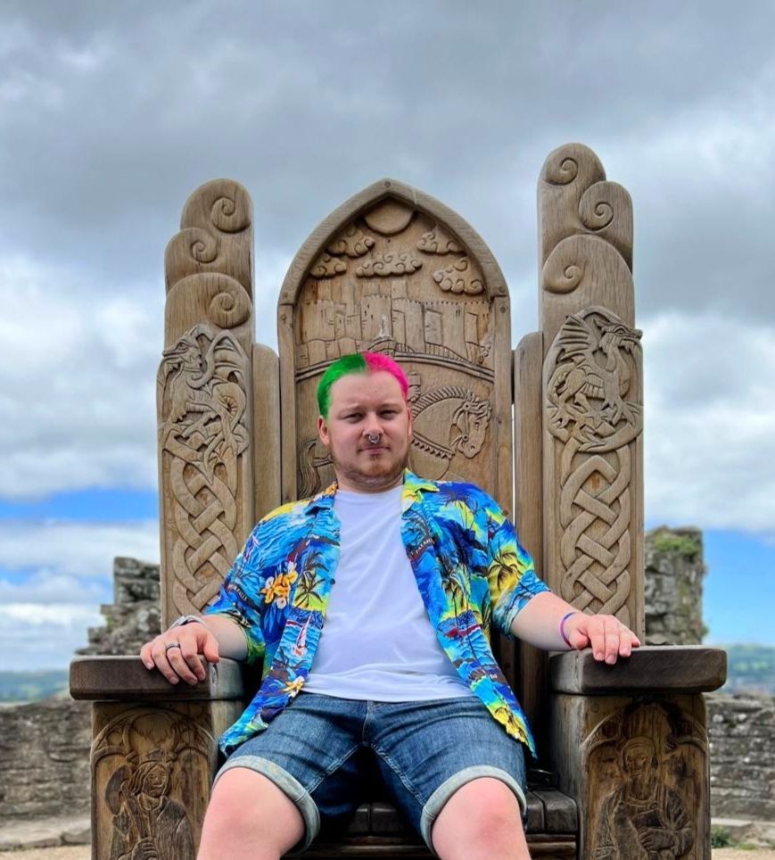 me, Gedds, a white guy with green and pink hair wearing jorts and an obnoxious blue short sleeved shirt