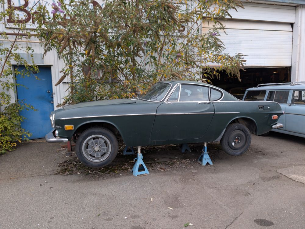 Green Volvo P1800 on supports outside of a volvo specialist