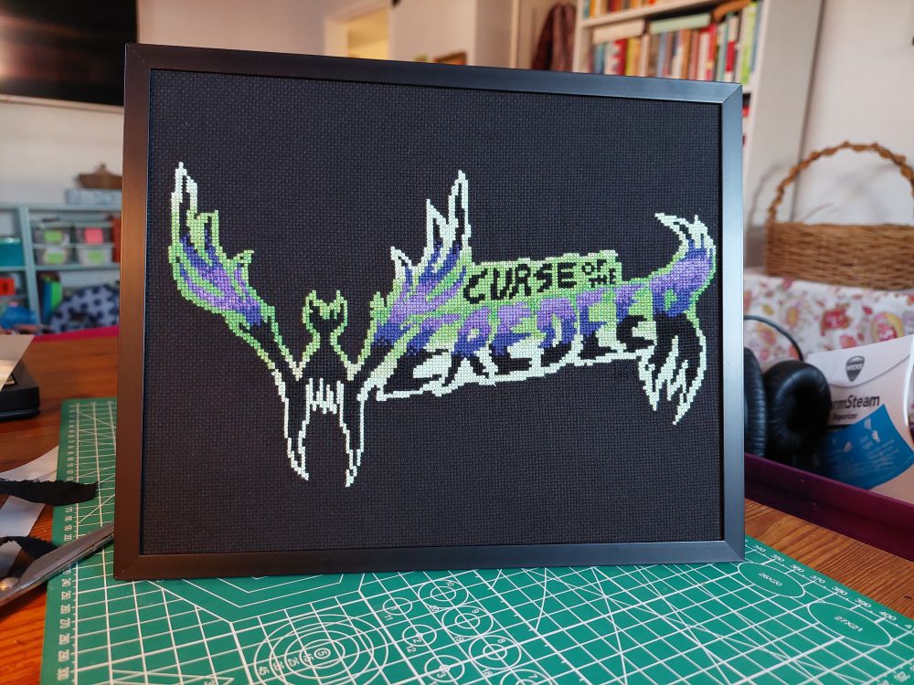 A framed cross-stitch of the logo for the movie Curse of the Weredeer