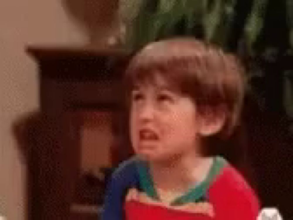 a young boy is making a funny face while sitting at a table in a living room .