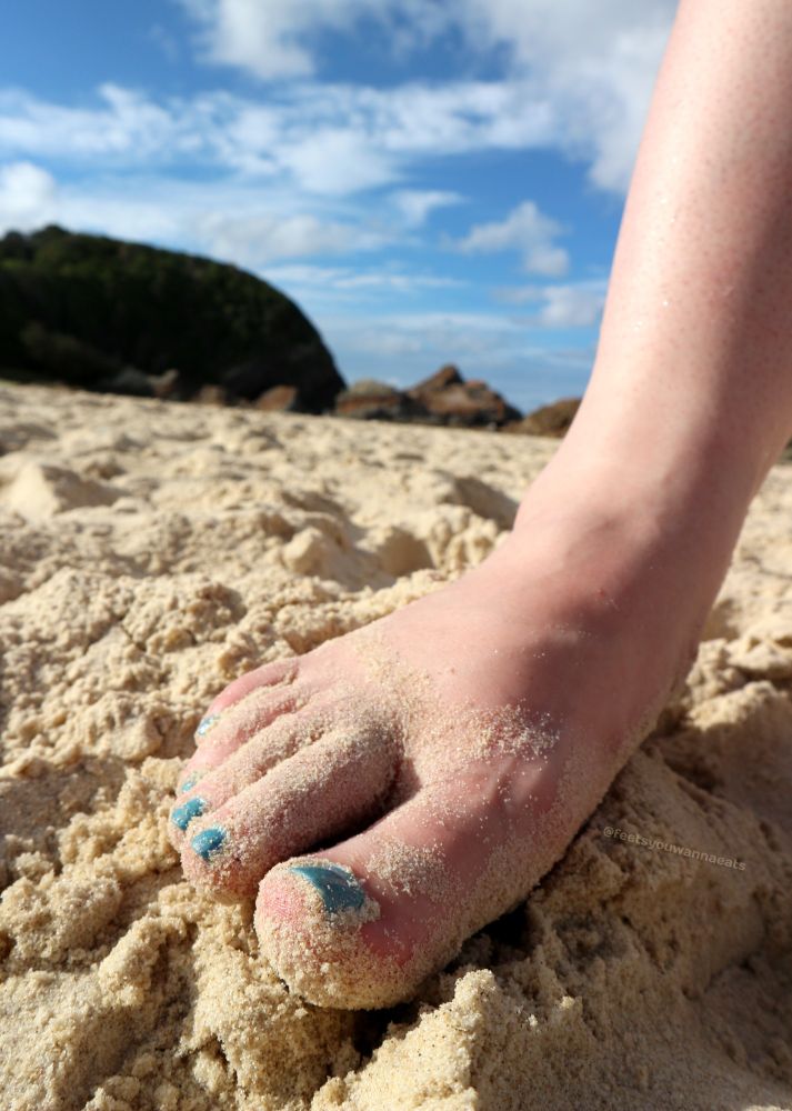 Close up of a lady's foot with blue nail polish in the sand on a sunny beach
