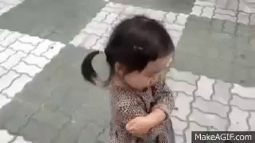 a little girl in a leopard print dress is standing on a brick sidewalk with her arms crossed .