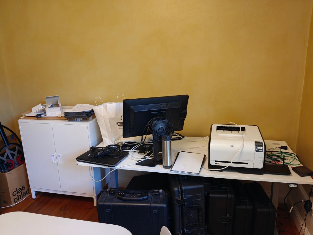 Stökigt skrivbord med en bildskärm, en skrivare och blandat jox