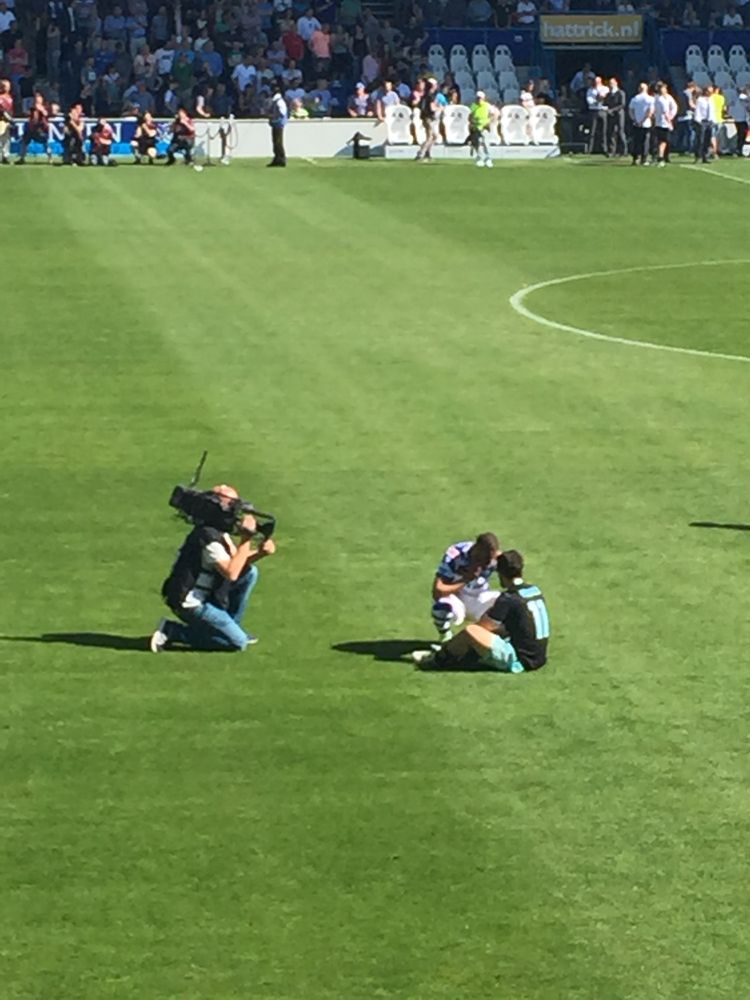 Younes zit verslagen op het gras in Doetinchem, in gesprek met een speler van de Graafschap, na het verliezen van het kampioenschap in mei 2016, terwijl een cameraman erbij geknield aan het filmen is 