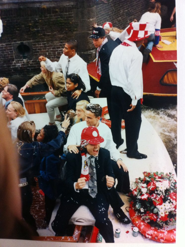 Jari Litmanen zit gebald met zijn vuisten met achter hem Mark Overmars. Op een rondvaartboot door de gracht, met feestende passagiers na winst Champions League 1995. Patrick Kluivert staat met hoge rood witte hoed naar het water te staren
