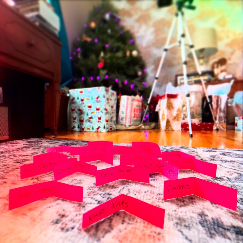 Various Christmas Movies on individual papers including Eyes Wide Shut, Batman Returns, Nutcrackers, Hot Frosty, Die Hard, Love Actually, Home Alone, This Christmas (aka Idris Elba Xmas), Last Christmas (aka Wham Christmas), it’s a Wonderful Life, and White Christmas