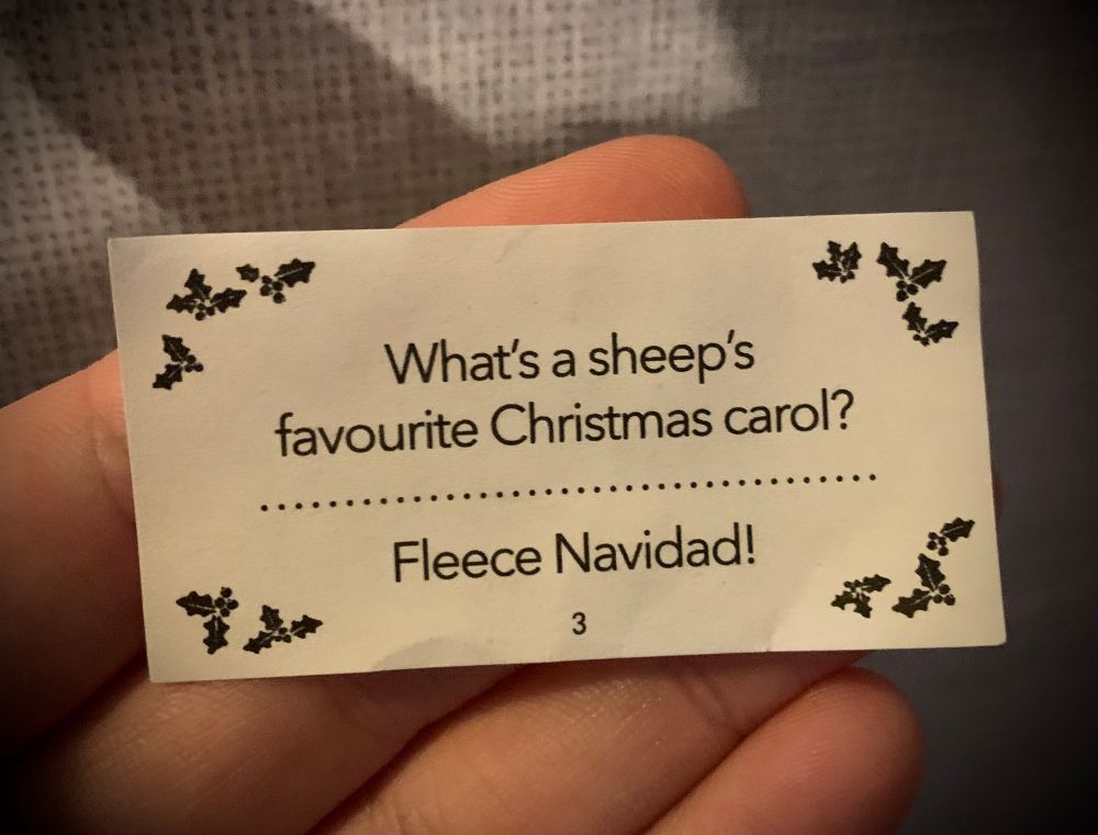 A Christmas cracker joke on a small piece of paper: what’s a sheep’s favourite Christmas carol? Fleece navidad!