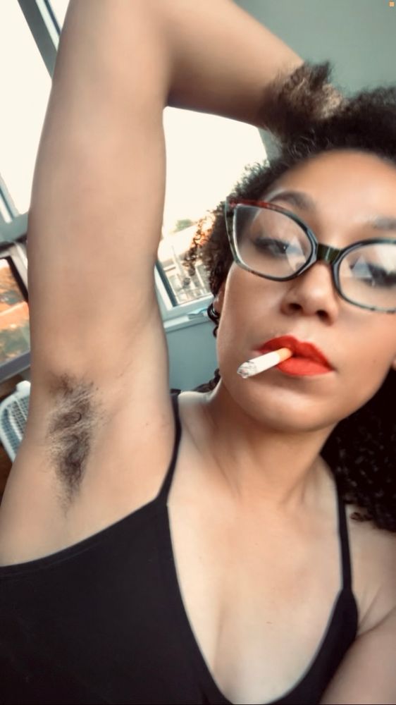 natou . looking at the camera w one arm behind their head and one hand behind their head.

he's wearing a black sports bra . cat eye glasses and red lipstick 