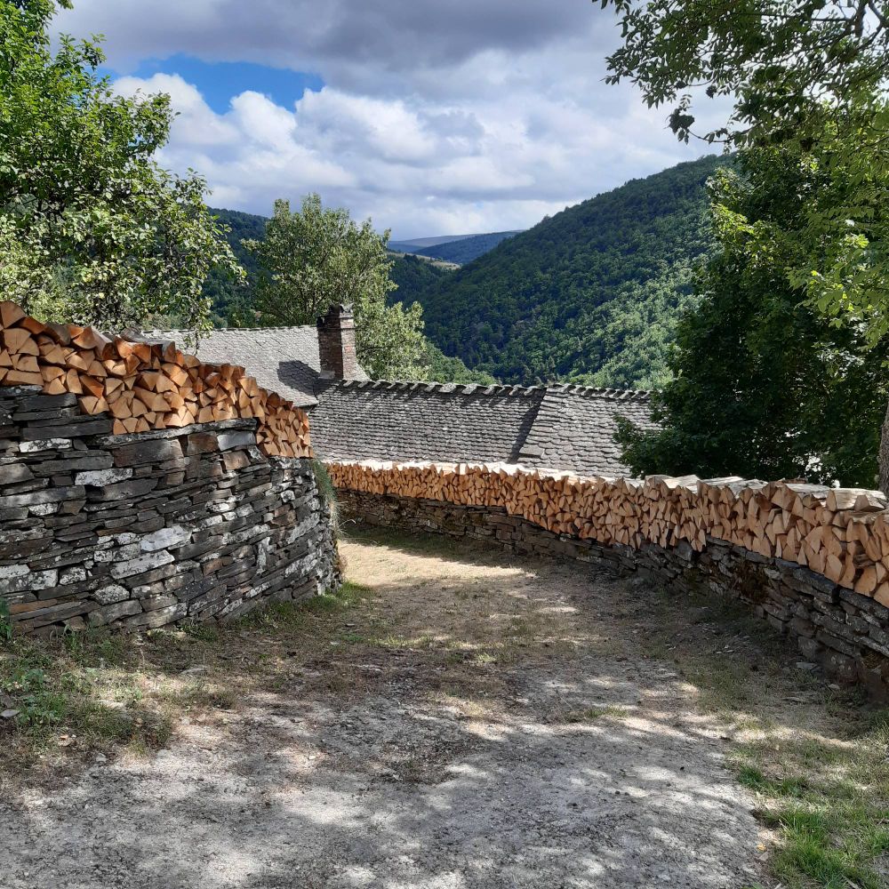 Murets en lauze surmontés de bûches de bois bien alignées 