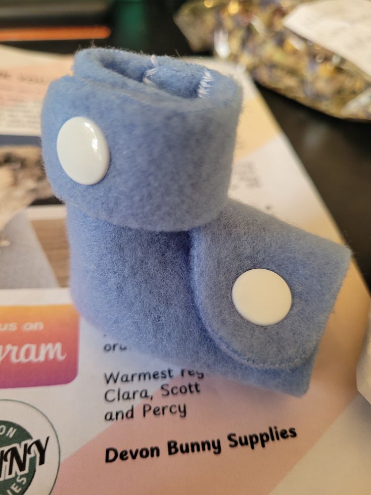 A blue foot wrap for a rabbit. It has white snap buttons. 