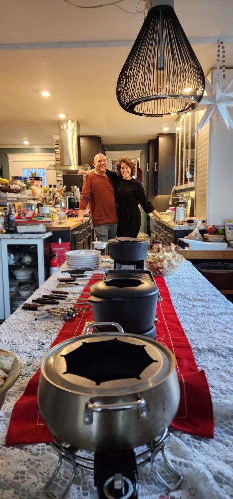Aaron and Caroline standing behind a full Christmas table of many fondue pots.