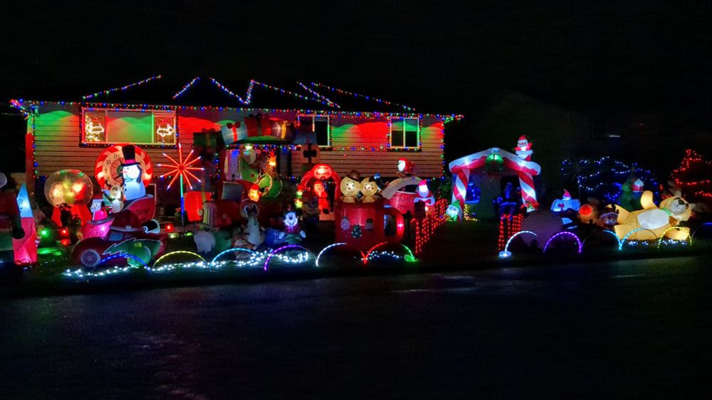 House covered in Christmas lights with a front lawn full of blow up Christmas figures, choreographed to music.
