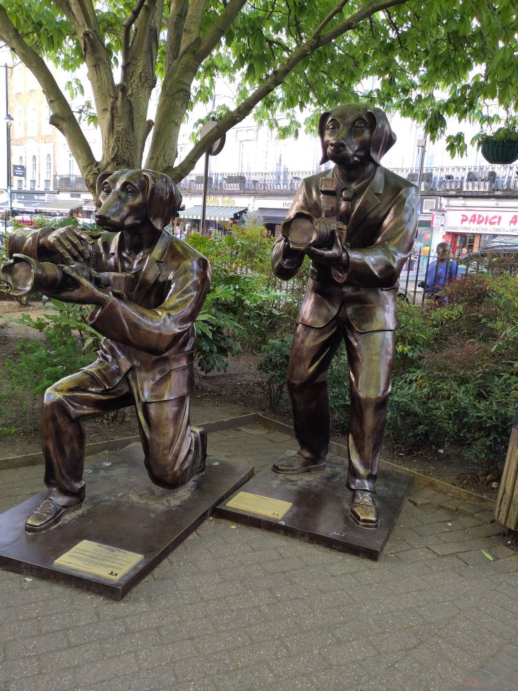 Two more bronze dog-men, both holding cameras. 
