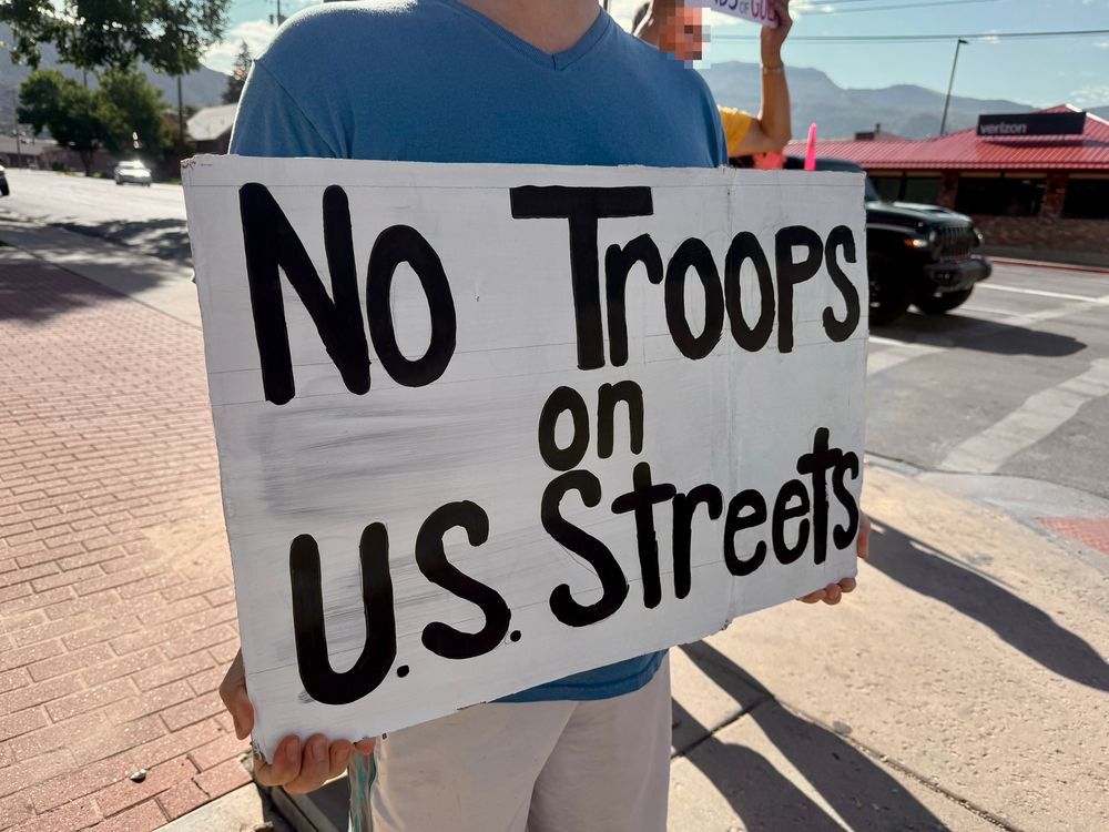 A protest sign held by a person at a street corner. 