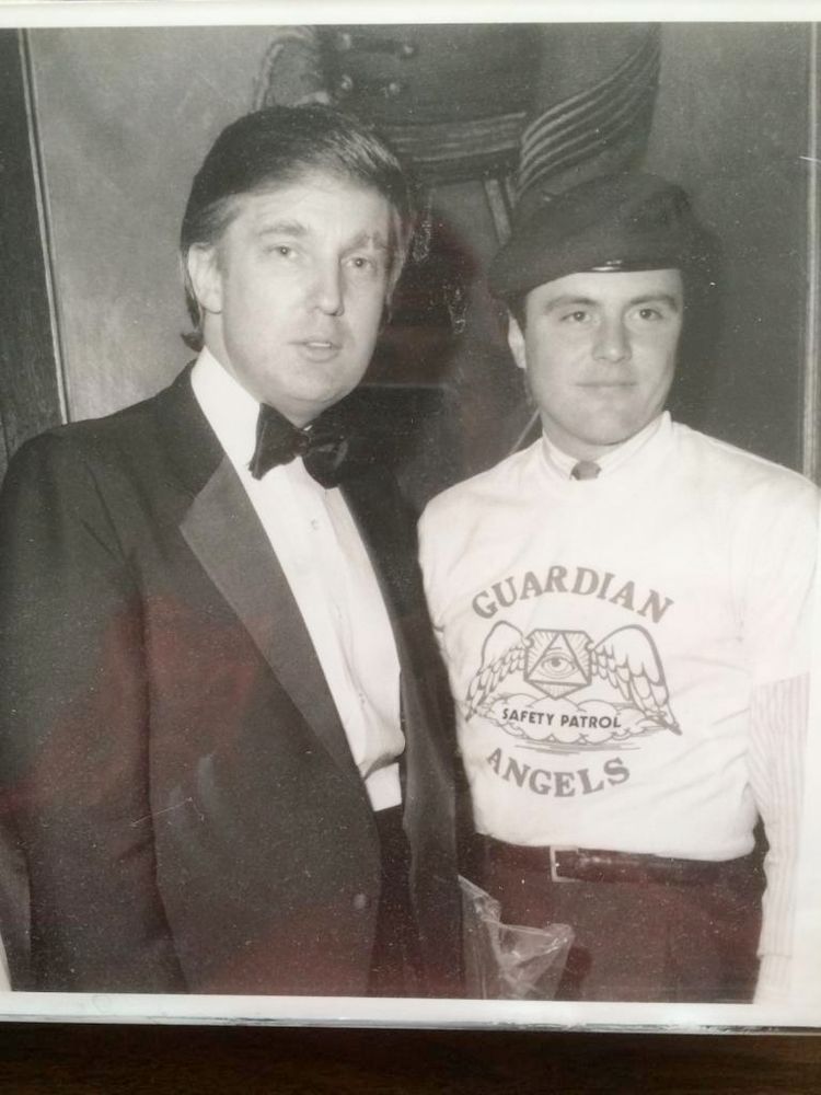 A photo, probably from an event in the 90s of Trump, in a tuxedo standing next to Sliwa in a beret, and wearing his Guardian Angels t-shirt over a collared shirt and tie. 