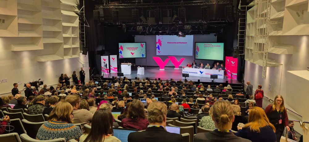 Sali täynnä väkeä. Lavalla vasemmiston logot