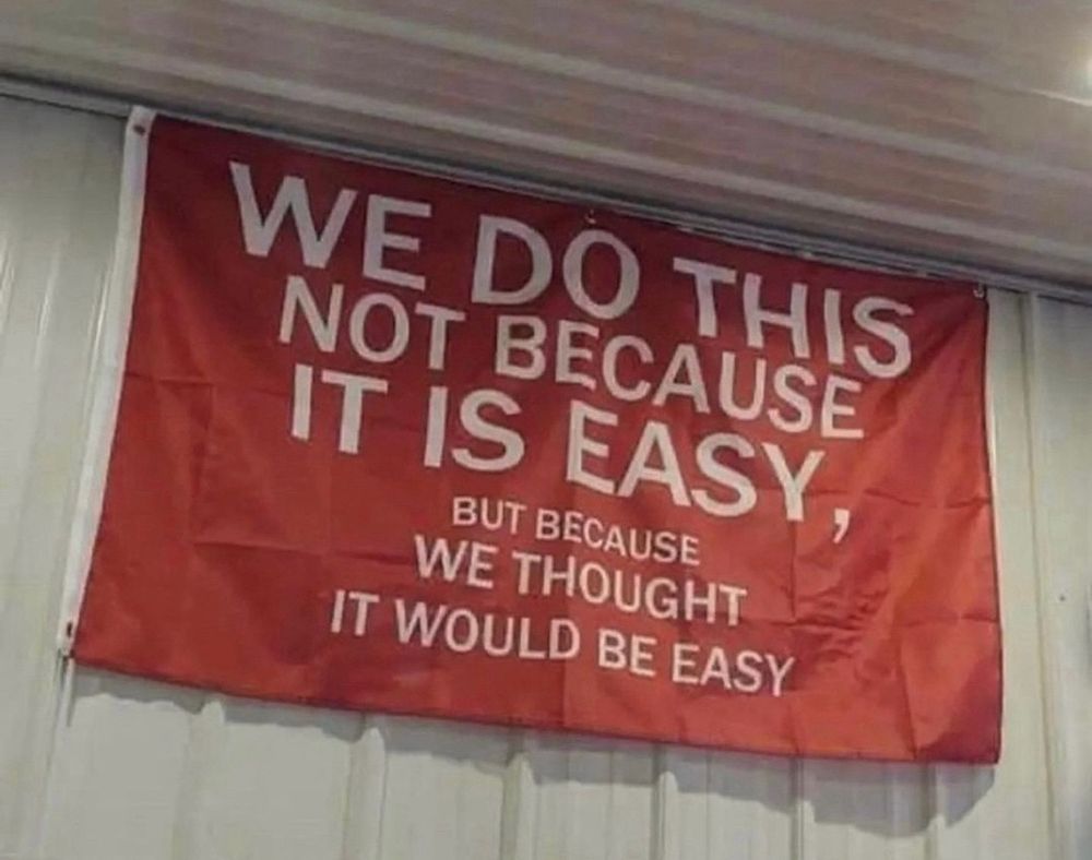 Flag that reads: 
We do this
Not because 
It is easy
But because
We thought
It would be easy
